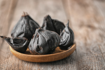 Plate with black garlic (Allium sativum) on wooden tableの写真素材