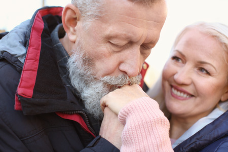 Mature man kissing his wife's hand outdoors, closeup