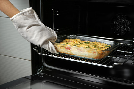 Woman taking glass baking dish with delicious casserole from oven, closeup
