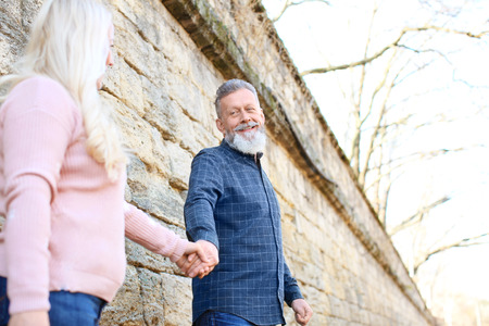 Happy mature couple holding hands near brick wall outdoorsの写真素材