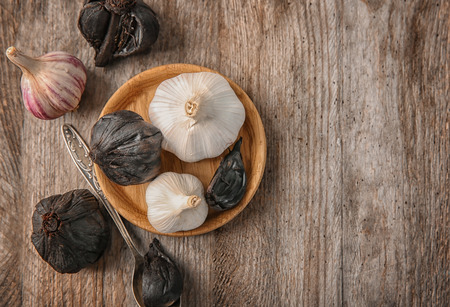 Plate with black (Allium sativum) and white garlic bulbs on wooden tableの写真素材