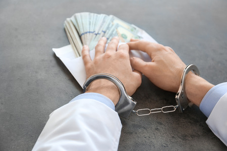 Doctor in handcuffs with bribe at workplaceの写真素材