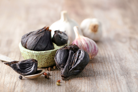 Black (Allium sativum) and white garlic bulbs on wooden tableの写真素材