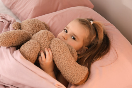 Cute little girl with teddy bear lying in bed at homeの写真素材