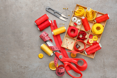 Colorful threads and sewing accessories on grey background