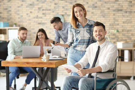 Young man in wheelchair with colleague at workplace