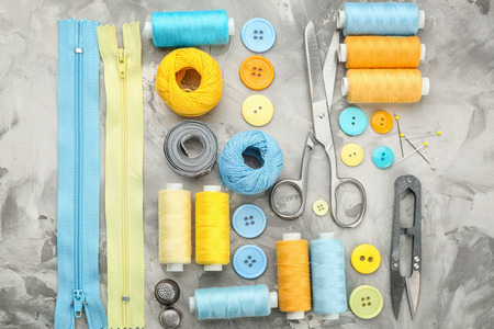 Colorful threads and sewing accessories on grey background