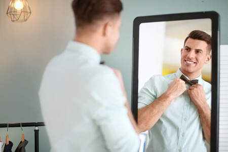 Man in new outfit looking at himself in mirror indoors. Fashionable wardrobeの写真素材