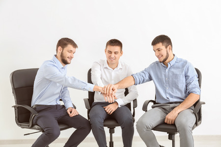 Young men putting hands together against white background. Unity concept