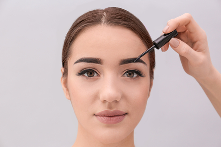 Young woman undergoing eyebrow correction procedure on light backgroundの写真素材