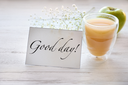 Glass of juice for breakfast and card with words "Good day" on tableの写真素材