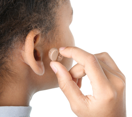 Little girl putting hearing aid in ear, closeup