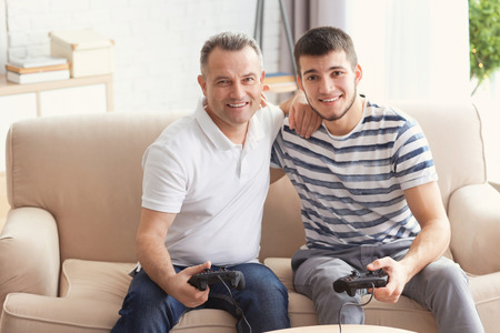 Mature man playing video game with his son at home