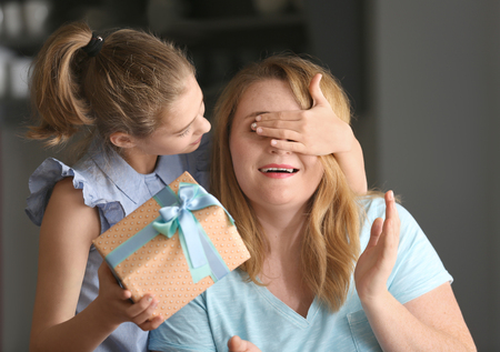 Cute little girl giving her mother a present at homeの写真素材