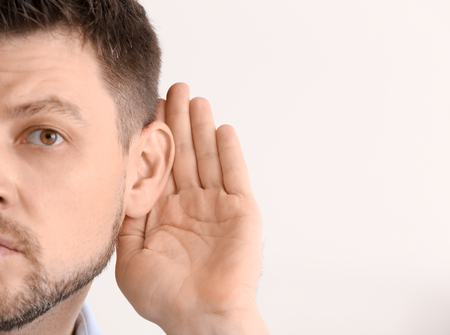 Mature man with hearing problem on light backgroundの写真素材
