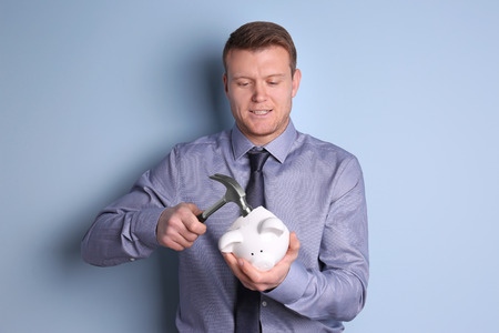 Young man holding hammer over piggy bank on color backgroundの写真素材