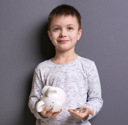 Cute boy holding broken piggy bank and coins on grey backgroundの写真素材
