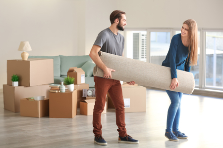 Young couple carrying carpet in room after moving to new homeの写真素材