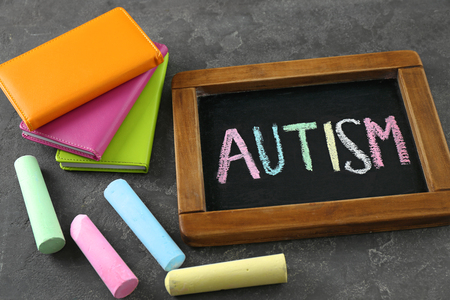 Blackboard with word AUTISM and pieces of chalk on grey backgroundの写真素材