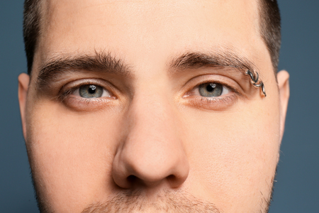 Young man with pierced eyebrow on color background, closeupの写真素材