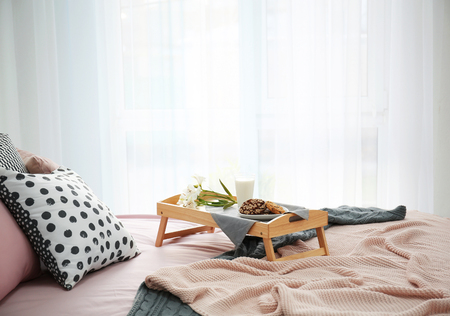 Tray with tasty breakfast and flowers on bedの写真素材