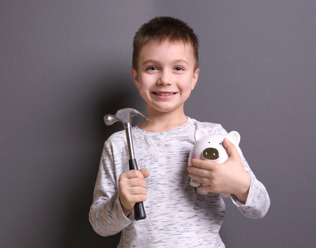 Cute boy holding hammer and piggy bank on grey backgroundの写真素材