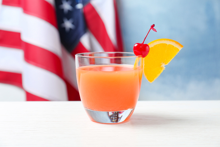 Glass with alcoholic cocktail on table against American flag backgroundの写真素材