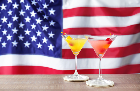 Glasses with alcoholic cocktails on table against American flag backgroundの写真素材