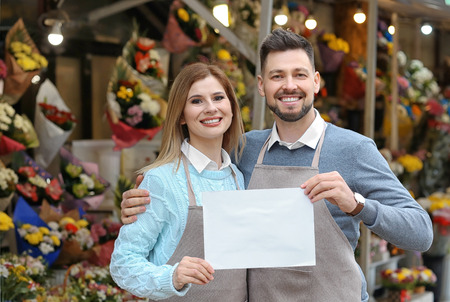 Business owners holding blank paper near their store with flowersの写真素材