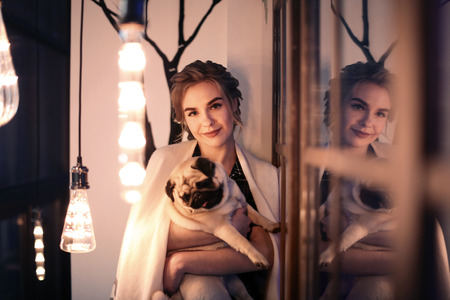 Young woman with cute pug dog near window at home. Pet adoptionの写真素材