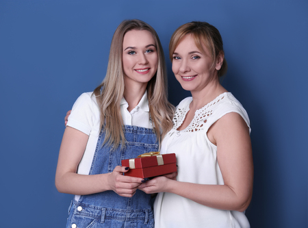 Young woman giving gift box to her mother on color backgroundの写真素材