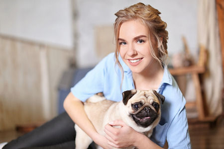 Young woman with cute pug dog at home. Pet adoptionの写真素材