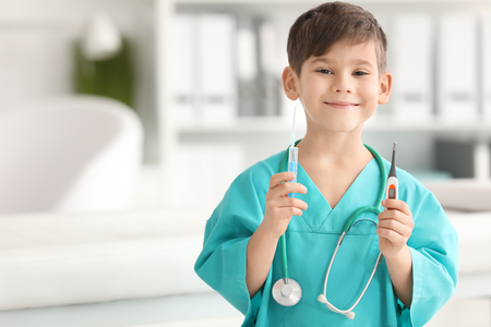 Cute little boy in doctor uniform and with medical instruments in hospitalの写真素材