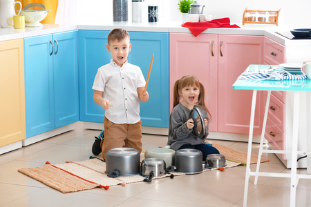 Cute little children playing with kitchenware as musical band at homeの写真素材