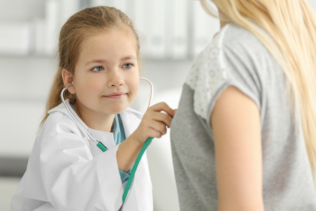 Cute little girl in doctor uniform examining patient indoorsの写真素材