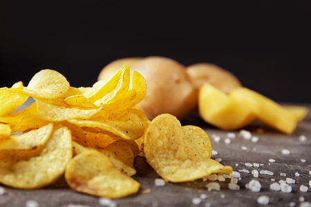 Yummy crispy potato chips with salt on grey table against dark backgroundの写真素材