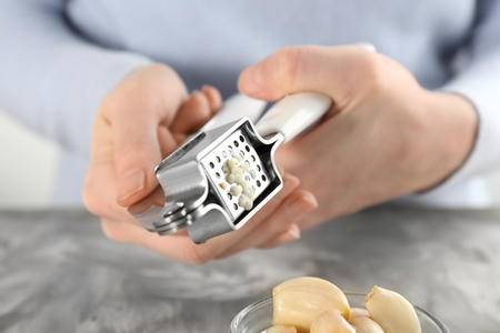 Woman crushing garlic with press at tableの写真素材