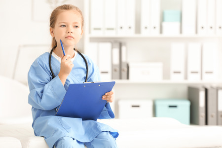 Cute little girl in doctor uniform with clipboard in hospitalの写真素材