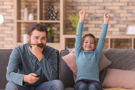 Father and daughter watching TV together at homeの写真素材