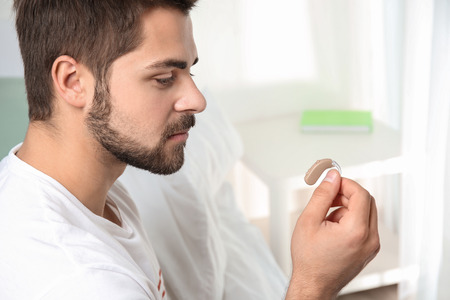 Young man holding hearing aid indoorsの写真素材