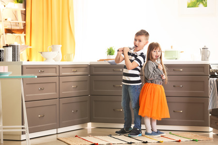 Cute little children using spoons as microphone in kitchenの写真素材