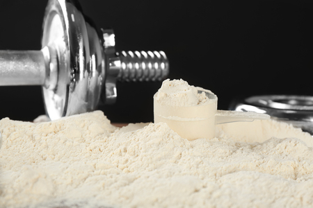 Heap of protein powder with scoop and dumbbell on tableの写真素材