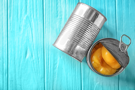 Cans with pickled apricots on wooden background