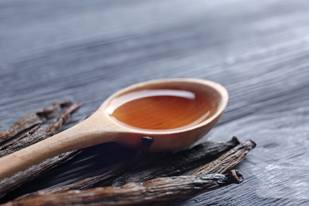 Spoon with vanilla extract and sticks on wooden backgroundの写真素材