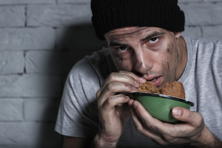 Hungry poor man eating piece of bread near brick wallの写真素材
