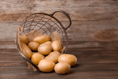 Overturned basket with fresh raw potatoes on wooden tableの写真素材