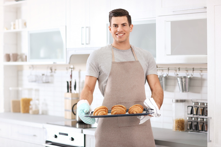 Man holding baking tray with delicious homemade croissants in kitchenの写真素材