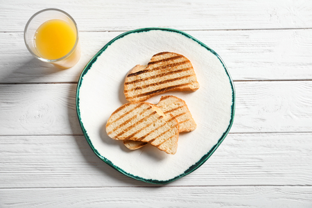 Plate with tasty toasted bread and glass of juice on tableの写真素材