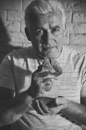 Poor man with little piece of bread on brick wall background. Black and white effectの写真素材