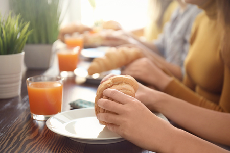 Women eating fresh croissants at table in cafeの写真素材